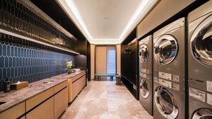 A modern laundry room with built-in washers and dryers, a marble countertop, and a bench.