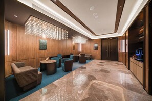 A modern lobby with a marble floor, seating area with sofas and armchairs, a fireplace, and a large chandelier.