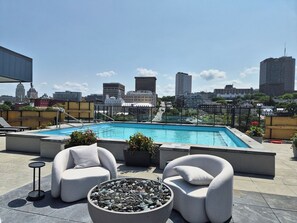 A rooftop pool with a cityscape view, two white cushioned chairs, a small round table, and a fire pit. - The Panorama · Sleeps 9 · 2 baths · EV parking (Québec City)