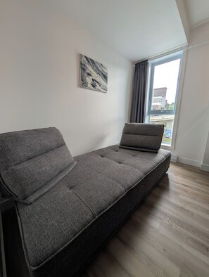 Ein modernes Wohnzimmer mit einem grauen Sofa, einem Marmorbild an der Wand und Blick auf eine Stadtlandschaft durch ein großes Fenster.