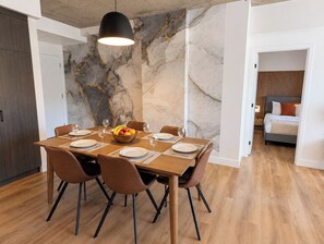 Een eetruimte met een marmeren wand, een houten tafel gedekt voor zes personen en een moderne hanglamp.