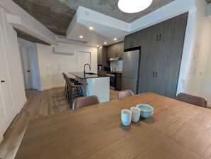 A modern kitchen with a central island, bar stools, a dining table with chairs, and a refrigerator. - The Panorama · Sleeps 9 · 2 baths · EV parking (Québec City)