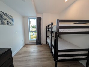 Een kamer met stapelbedden, een raam met gordijnen, een houten vloer en een kunstwerk aan de wand.