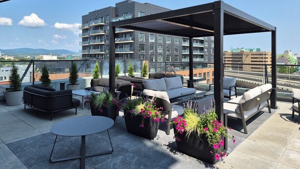 Een terras op het dak met buitenmeubels, plantenpotten en uitzicht op een stadsbeeld.