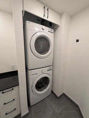A laundry room with two stacked white LG washing machines, a black countertop, and a white wall with a black electrical outlet. - The Zenith · Sleeps 8 · 11th fl · EV parking (Québec City)