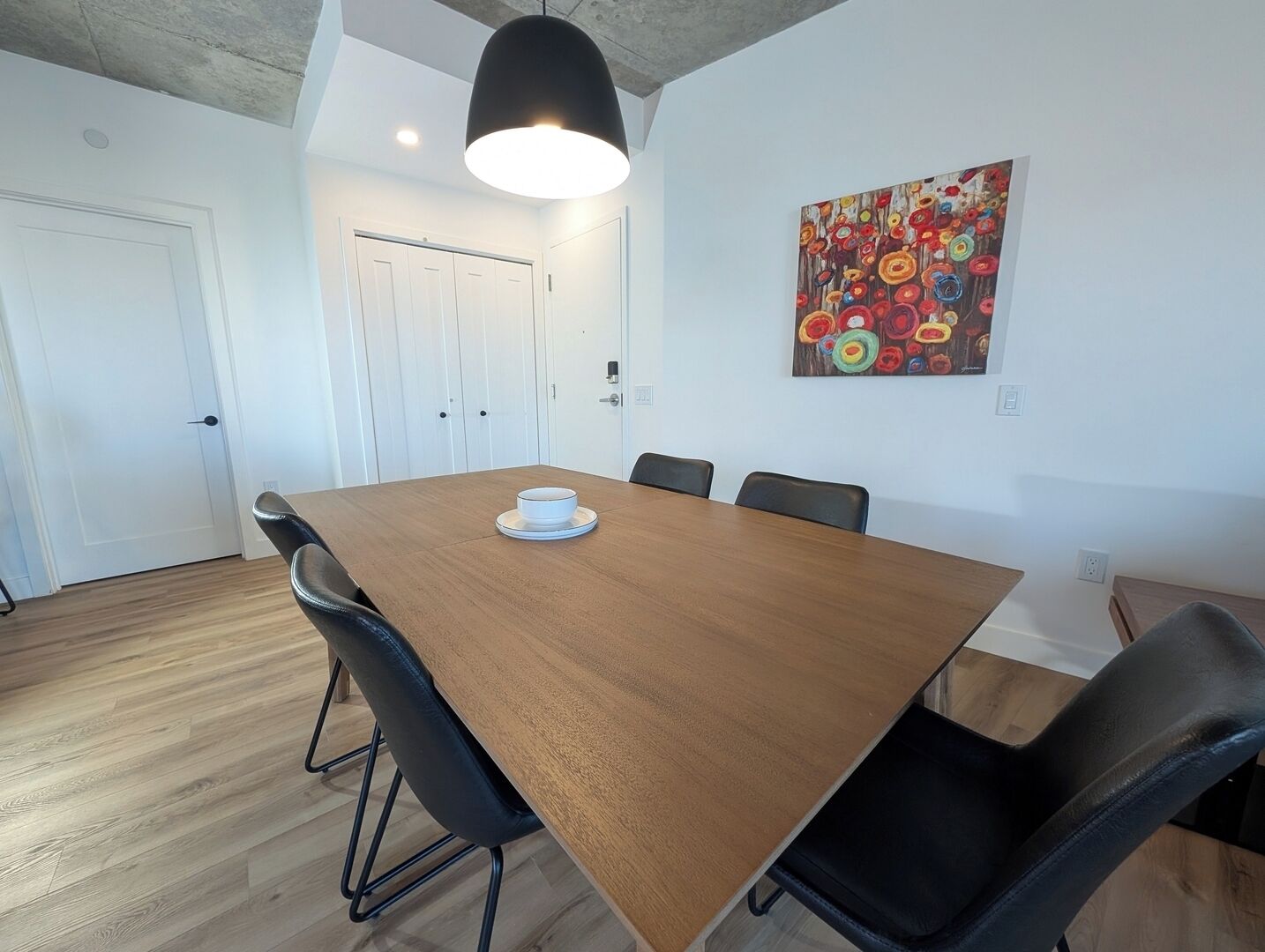 Un salón de conferencias con una mesa de madera, sillas negras, una puerta blanca y un cuadro abstracto de colores en la pared.