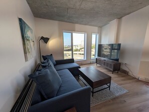 A modern living room with a sectional sofa, a flat-screen TV, and large windows. - The Zenith · Sleeps 8 · 11th fl · EV parking (Québec City)