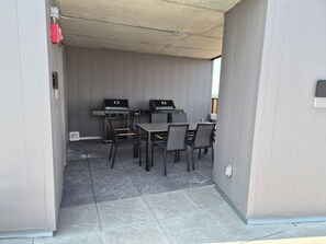 Ein Außenbereich mit einer Terrasse, zwei Grillstationen, einem Tisch und vier Stühlen.