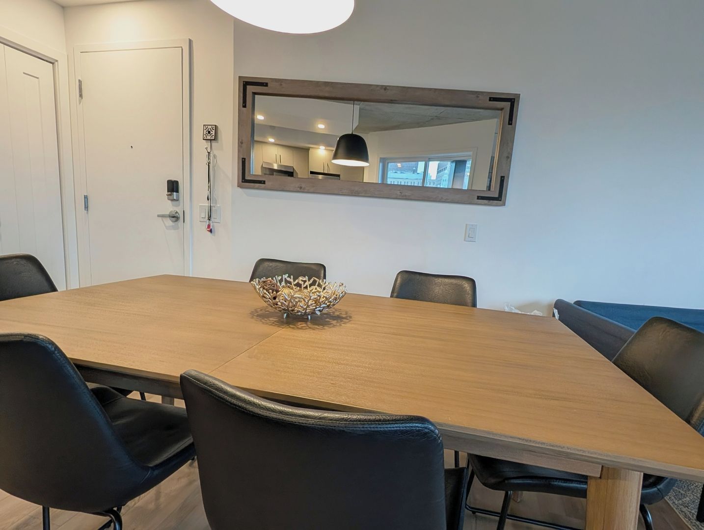 Une salle de conférence avec une table en bois, des chaises noires, un vase décoratif et un grand miroir au mur.
