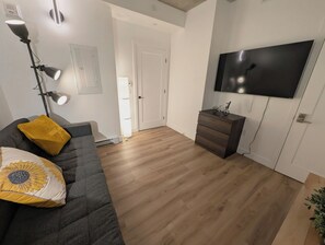 A modern living room with a grey sofa, a yellow pillow, a floor lamp, a TV on the wall, and a wooden cabinet. - The Zenith · Sleeps 8 · 11th fl · EV parking (Québec City)