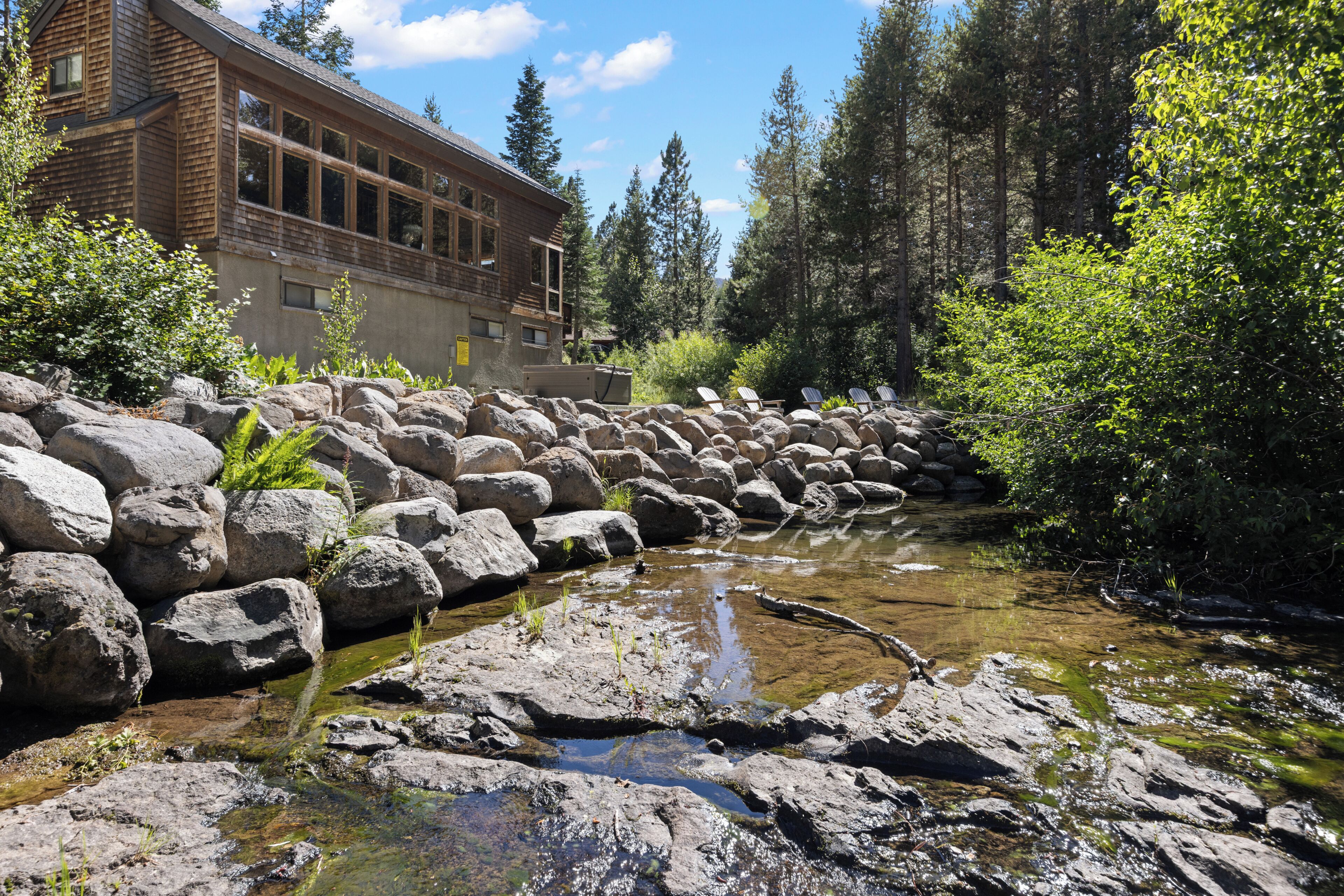 Paisaje natural con un arroyo, rocas y un edificio con ventanas grandes.