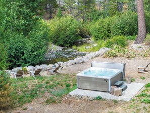 An outdoor hot tub with a stone surround, a wooden deck, and a river in the background.
