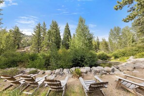 A natural outdoor setting with a stone wall, wooden Adirondack chairs, and a variety of trees.