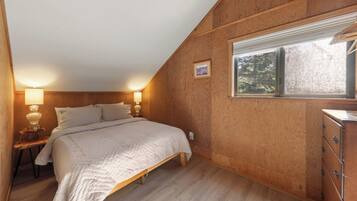 A bedroom with a bed, bedside lamps, a dresser, and a window with a view of trees.
