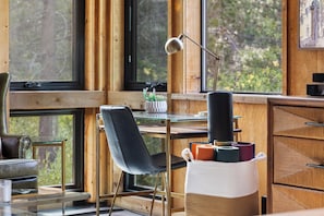 A modern room with a desk, chair, lamp, and a view of greenery outside.