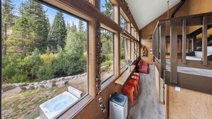 Ein Zimmer mit großen Fenstern mit Blick auf einen Wald, einer Whirlpool und einer Sitzecke mit roten Stühlen.