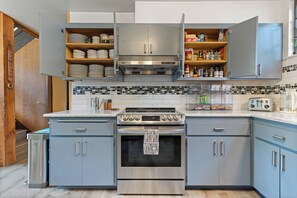 A modern kitchen with stainless steel appliances, wooden shelves, and a tiled backsplash.