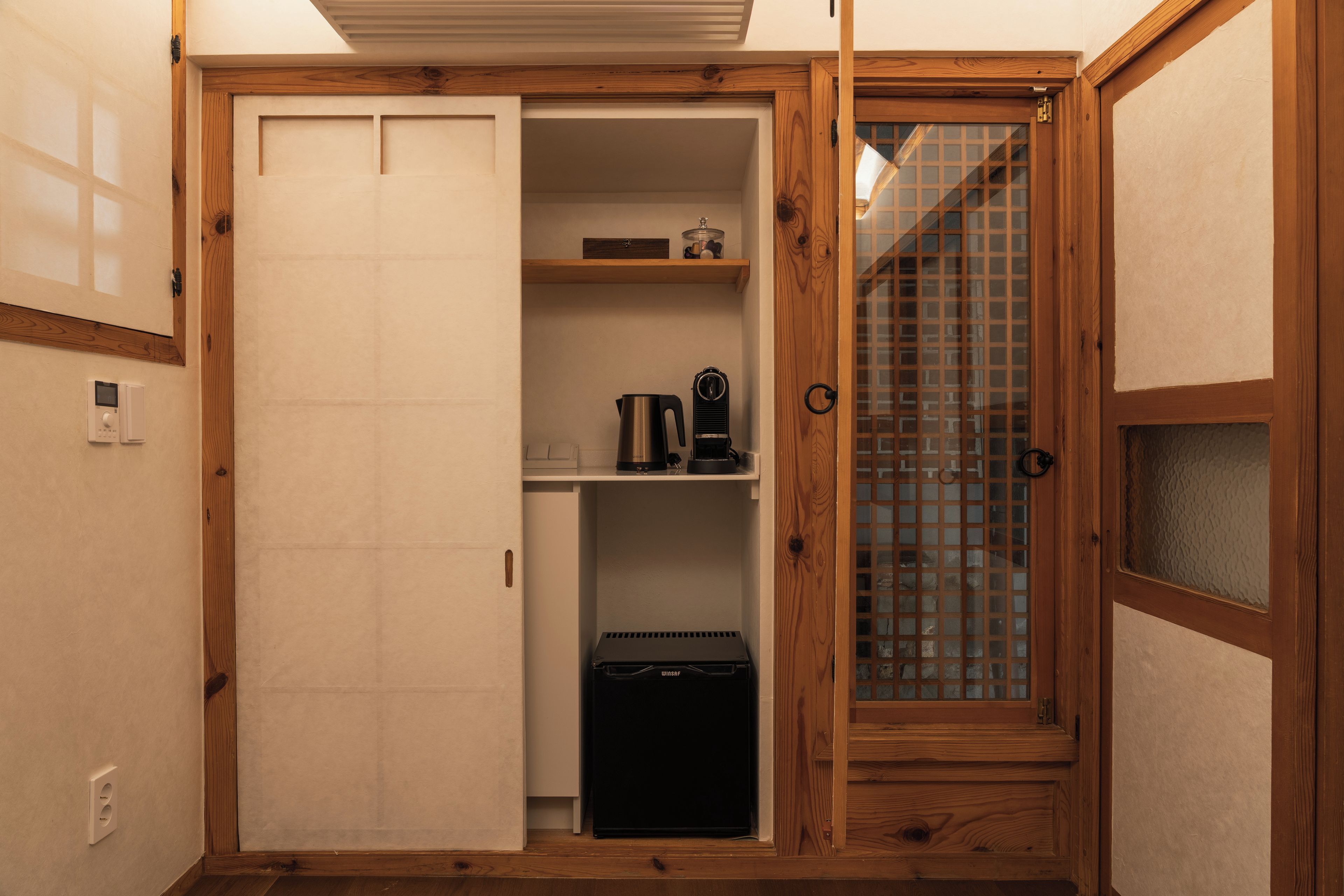 A compact room with a wooden cabinet, a small black appliance, and a window with a grid pattern.
