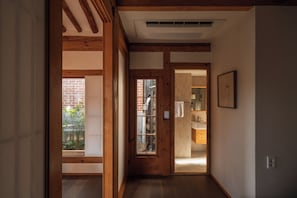 A hallway with wooden beams, a door leading to a bathroom, and a window with a view of a brick wall and greenery. - The Prima Hotel Hanok Dambakjae Gyedong (Seoul)