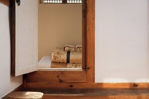 A traditional Japanese room with tatami flooring, a low wooden bench, and a bed with floral bedding.