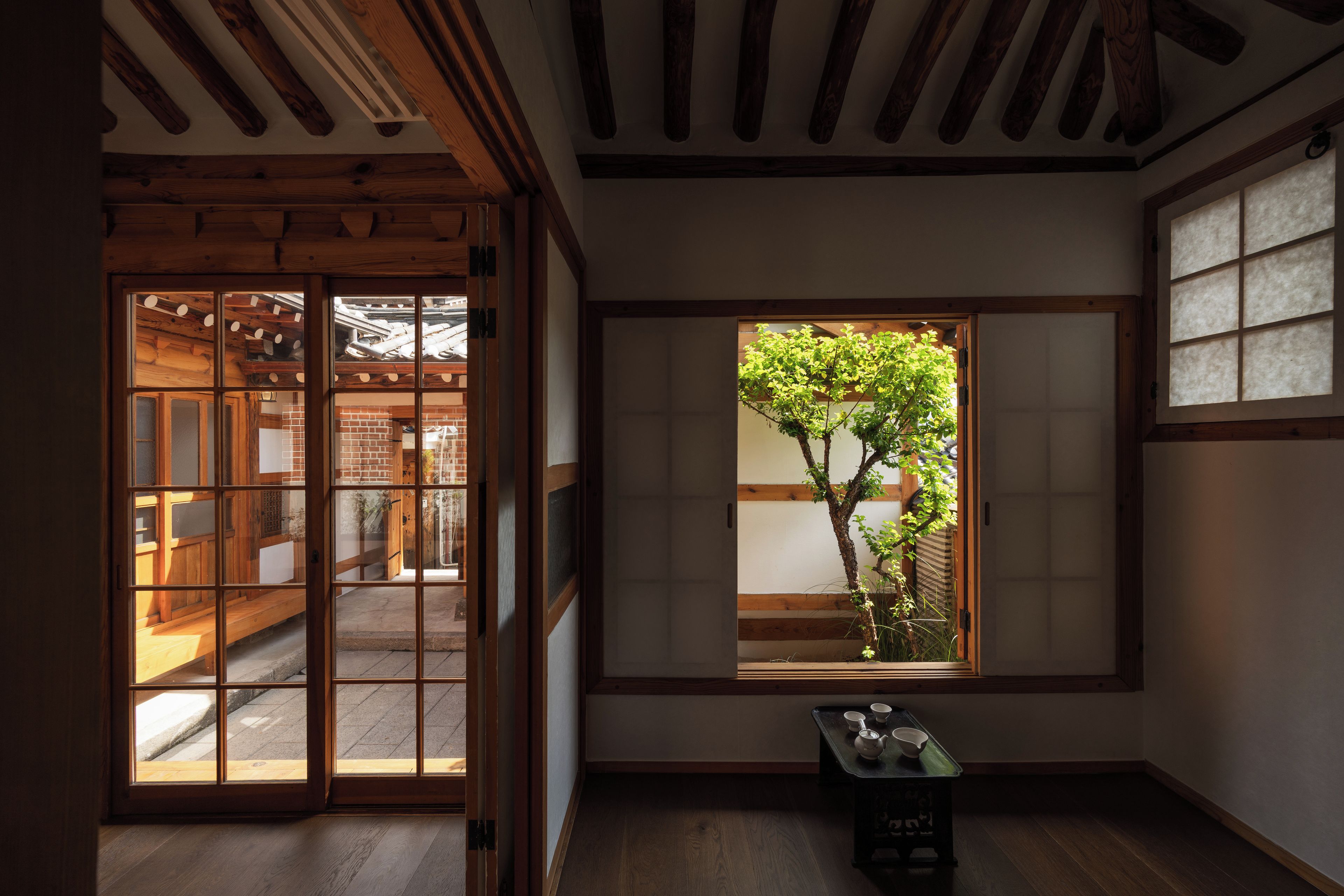 A traditional Japanese room with sliding doors, a window with a view of a tree, and a small table with tea set.