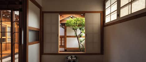 Una habitación tradicional japonesa con suelo de tatami, puertas correderas y vistas a un árbol desde una ventana.