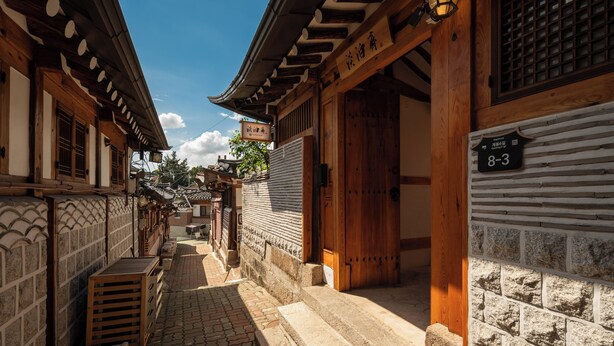 Un callejón tradicional coreano con edificios de madera, paredes de azulejos y un letrero que indica la habitación número 8-3.