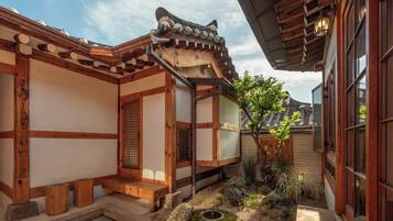A traditional Korean-style building with wooden beams, tiled roofs, and a small garden area with a tree and a stone lantern.