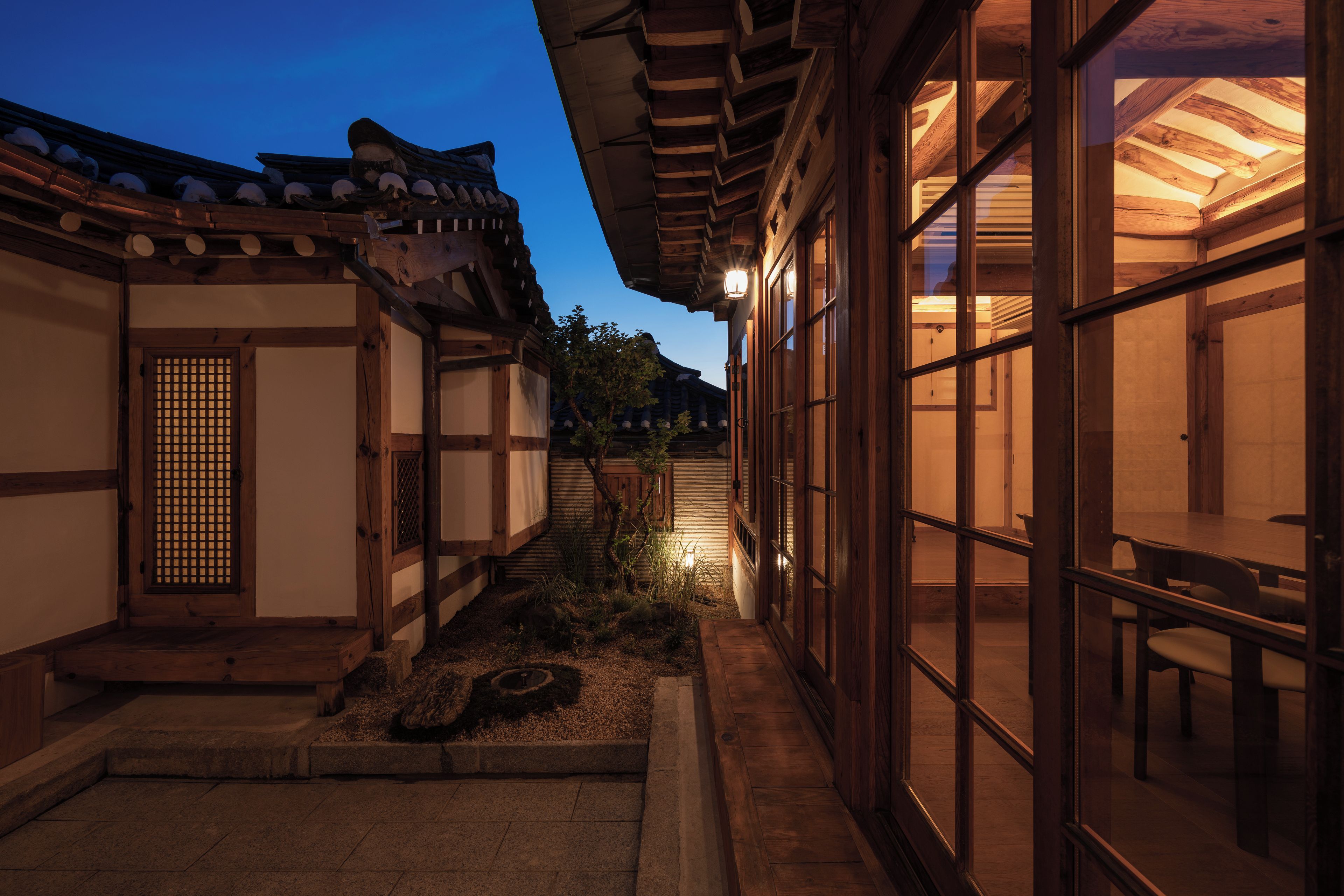 Un edificio japonés tradicional con fachada de madera, techo de tejas y un pequeño jardín con un farol de piedra.