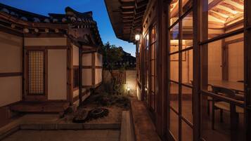 Un edificio japonés tradicional con fachada de madera, techo de tejas y un pequeño jardín con un farol de piedra.
