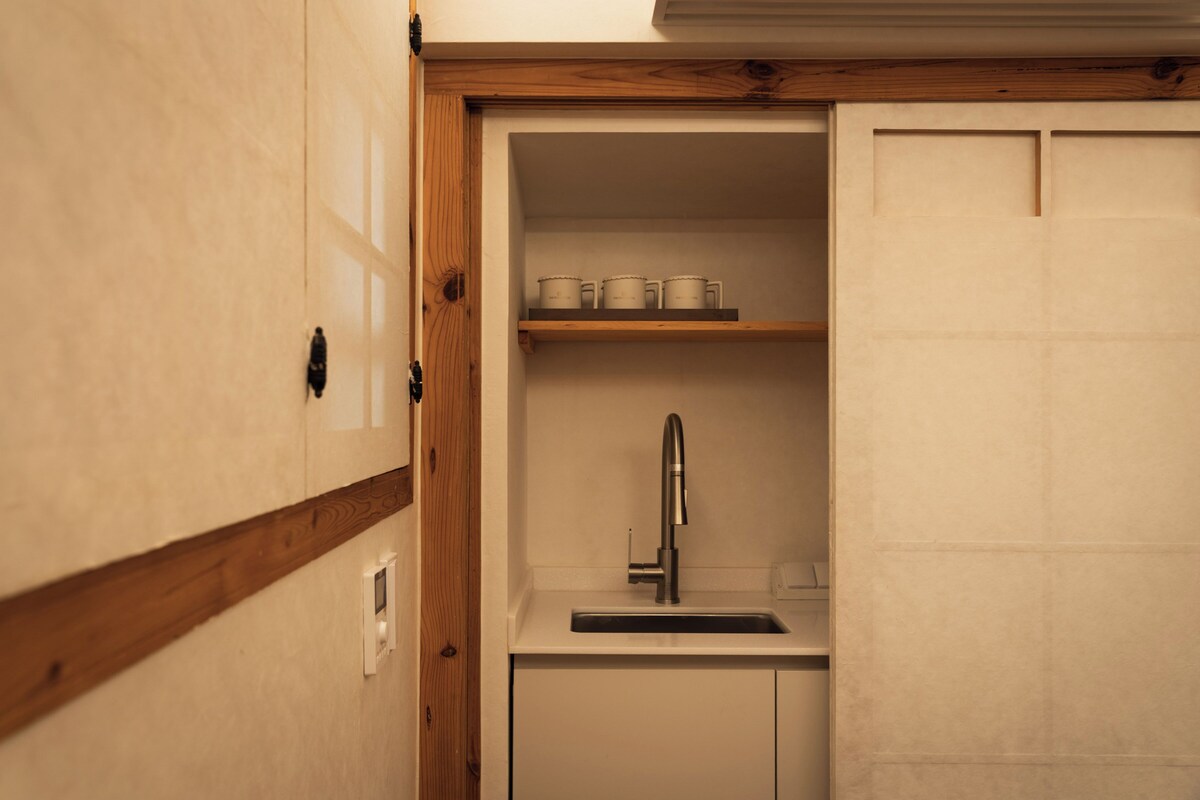 A compact kitchen with a built-in sink, wooden shelves, and a white countertop.