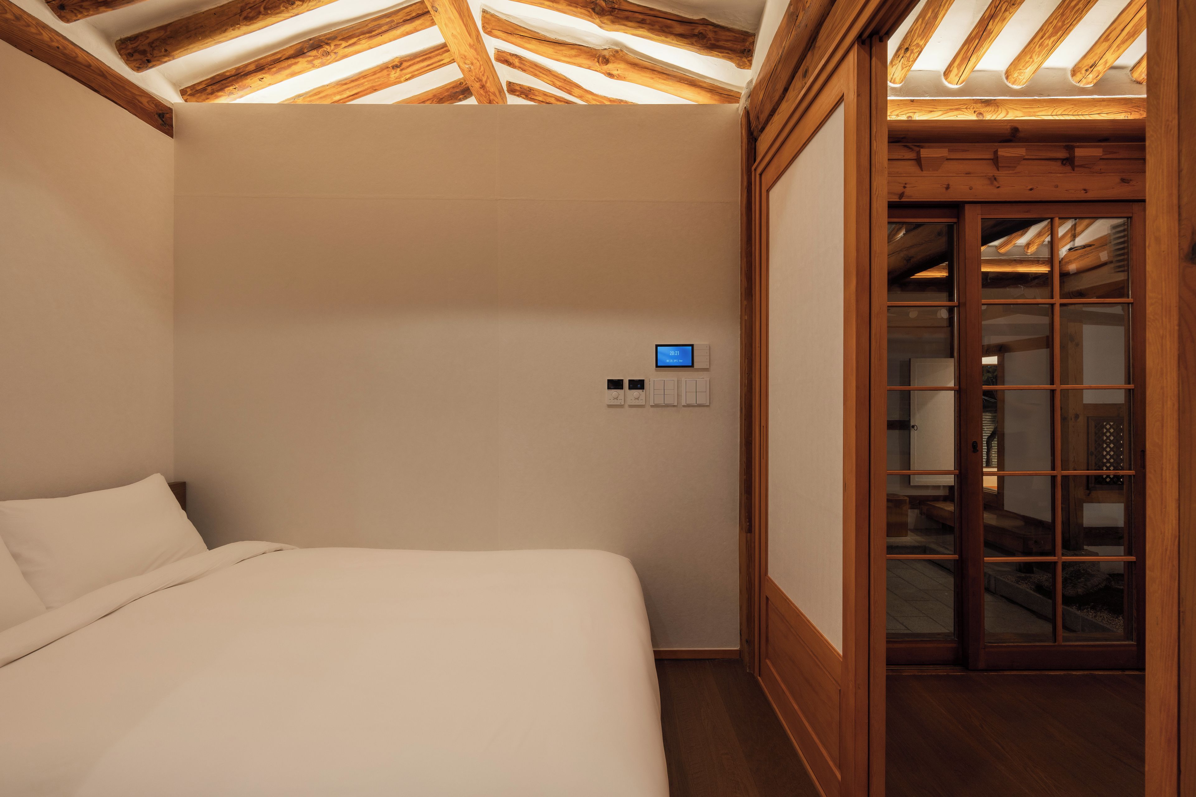 A bedroom with a wooden ceiling, a bed, and a digital clock on the wall.