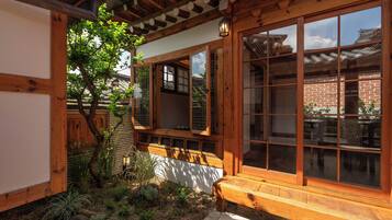 Un bâtiment de style japonais traditionnel, avec des poutres en bois, des portes coulissantes et un petit jardin agrémenté d’un banc et de plantes.