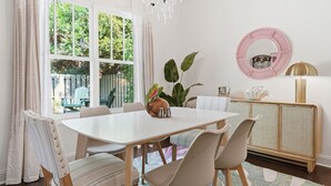Un'area pranzo con un tavolo bianco, sedie a righe, un lampadario e vista sul verde circostante.