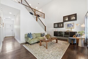 A spacious living room with a staircase, a sofa, a coffee table, and a TV. - Cypress Blue - Turo Rental Available (Southern Pines)