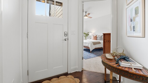 Una porta bianca con una finestra, una ventola a soffitto e un tavolino con libri e una ciotola.