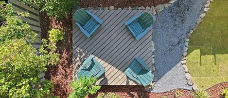 A top-down view of a patio area with a wooden deck, four green Adirondack chairs, and surrounding landscaping.