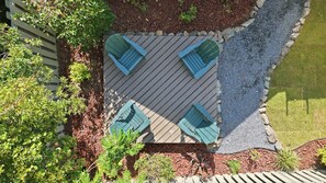 A top-down view of a patio area with a wooden deck, four green Adirondack chairs, and surrounding landscaping. - Cypress Blue - Turo Rental Available (Southern Pines)