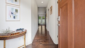 Un corridoio con pavimento in legno, una porta di legno e opere d'arte astratte incorniciate al muro.