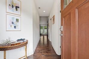 A hallway with wooden flooring, a wooden door, and framed abstract art on the wall. - Cypress Blue - Turo Rental Available (Southern Pines)