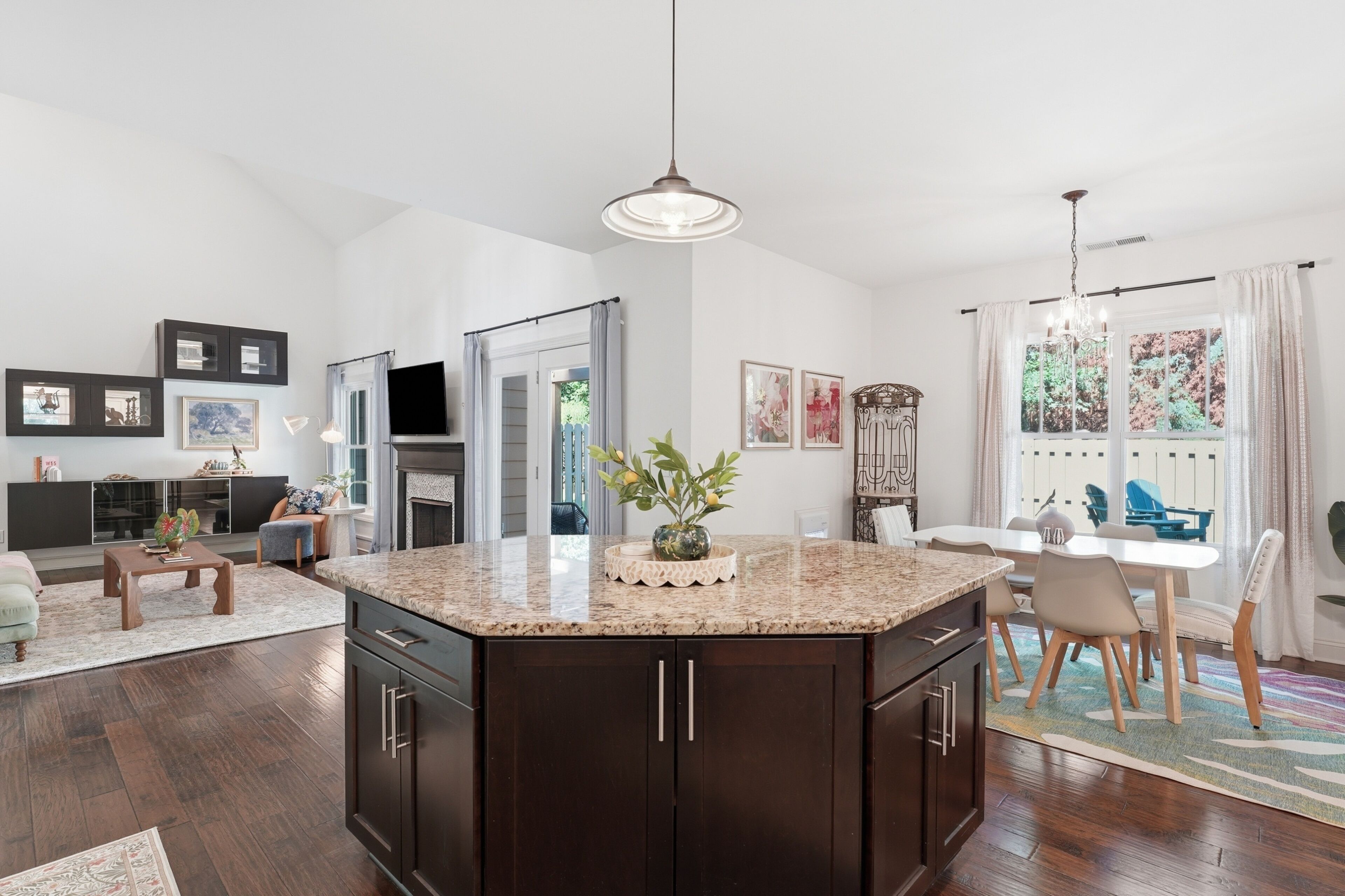 A modern kitchen with a large island, dark cabinetry, and a dining area with a table and chairs.
