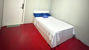 A small, single-bed room with a red floor, white walls, and a ceiling fan. - SJD Sagana Resort (Macarthur)