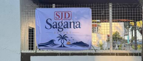 Banner para SJD Sagana Resort con diseño tropical, incluyendo palmeras y olas.