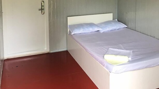 A single-bed room with a white headboard, a door with a handle, and a ceiling light fixture. - SJD Sagana Resort (Macarthur)