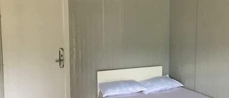 Habitación individual con una cama y cabecera blanca, una puerta con picaporte e iluminación en el techo.