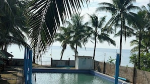 A swimming pool with a tiled edge, surrounded by palm trees and a view of the sea. - SJD Sagana Resort (Macarthur)