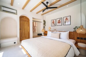 A bedroom with a large bed, wooden ceiling beams, a ceiling fan, and wall-mounted artwork. - Villa Raya & Villa Viora Uluwatu (Pecatu)