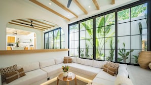 Una sala de estar moderna con un amplio sofá modular, una mesita de centro y vistas a un exuberante follaje a través de amplios ventanales.