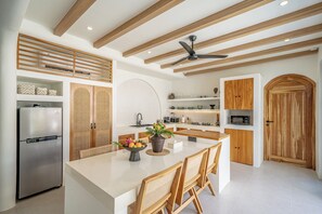 A modern kitchen with a central island, wooden beams, and built-in appliances. - Villa Raya & Villa Viora Uluwatu (Pecatu)