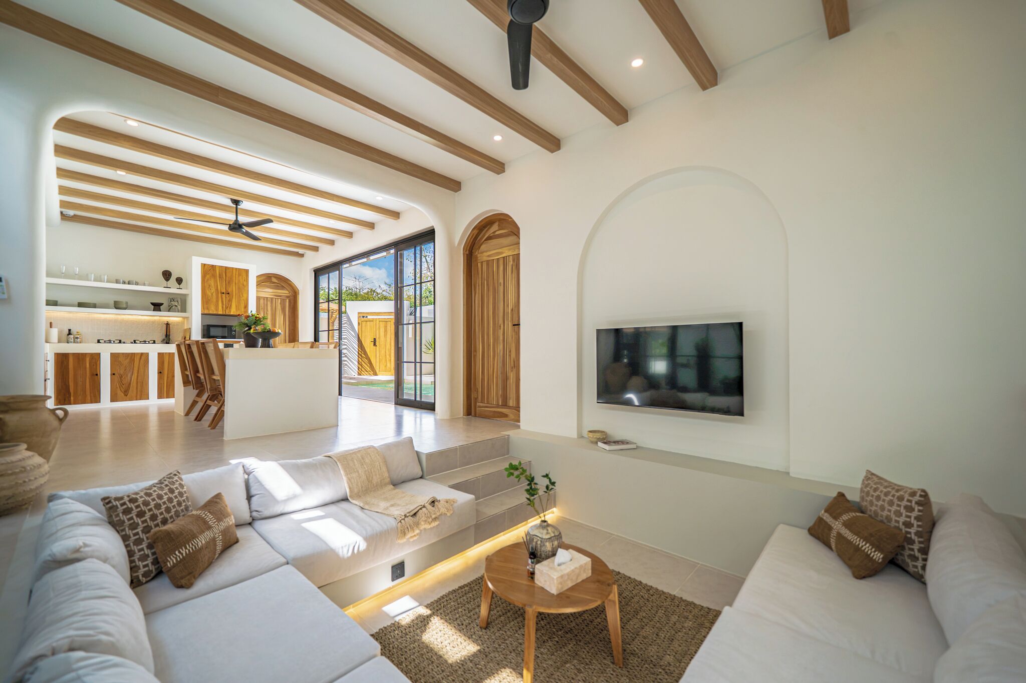 A spacious living area with a sofa set, a coffee table, and a TV mounted on the wall.
